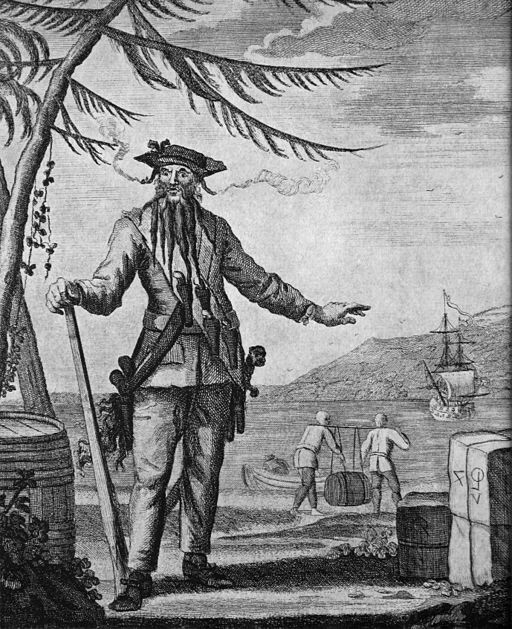 18th-century engraving of the pirate Blackbeard standing on a shore with smoke curling from his beard while his crew unloads barrels from a ship in the background.